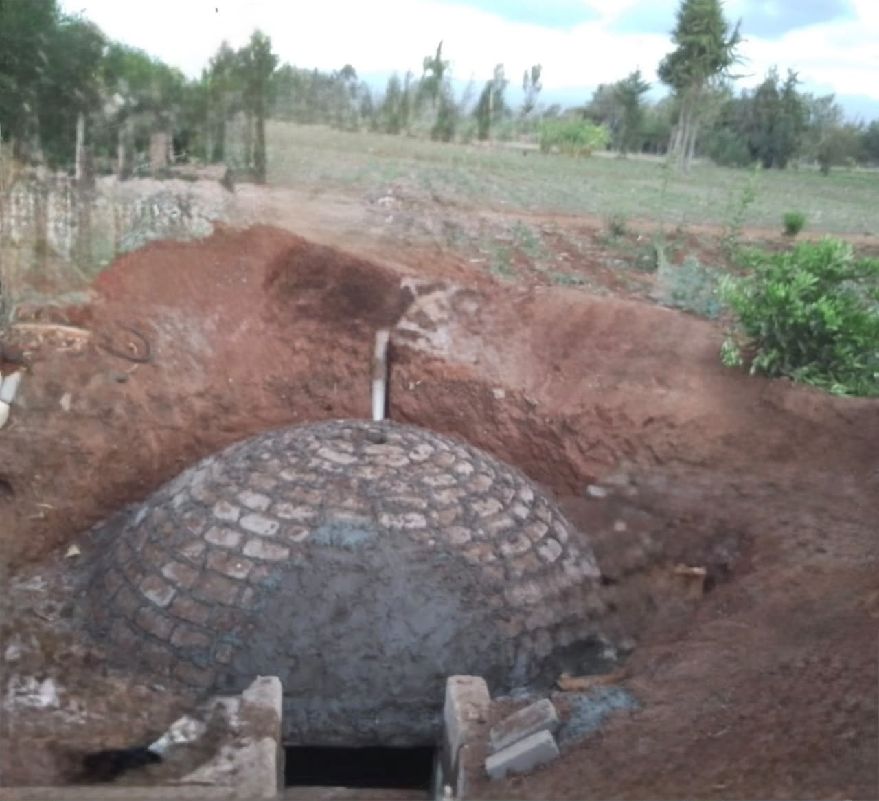 Brick dome biodigester under construction in open trench with inlet pipe
