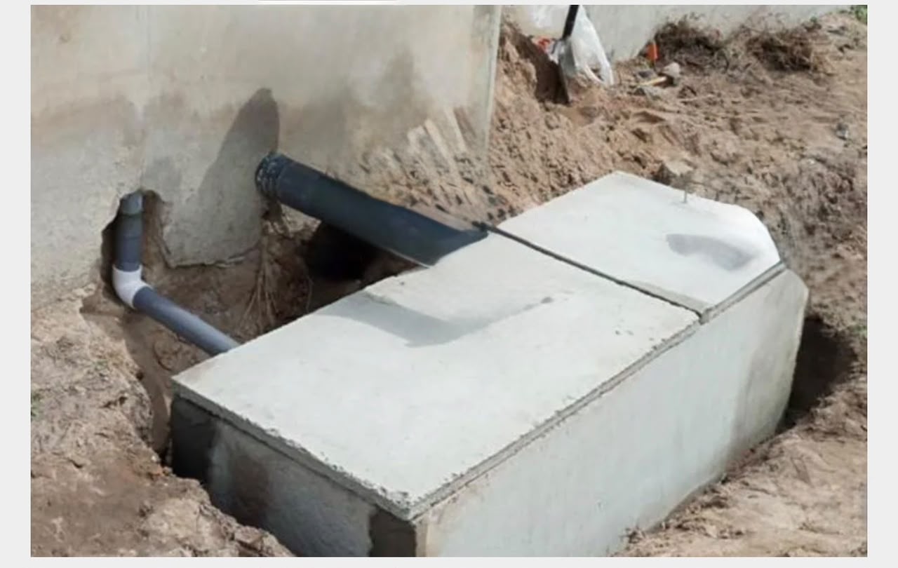 Concrete biodigester tank in trench with PVC pipes connected to building wall